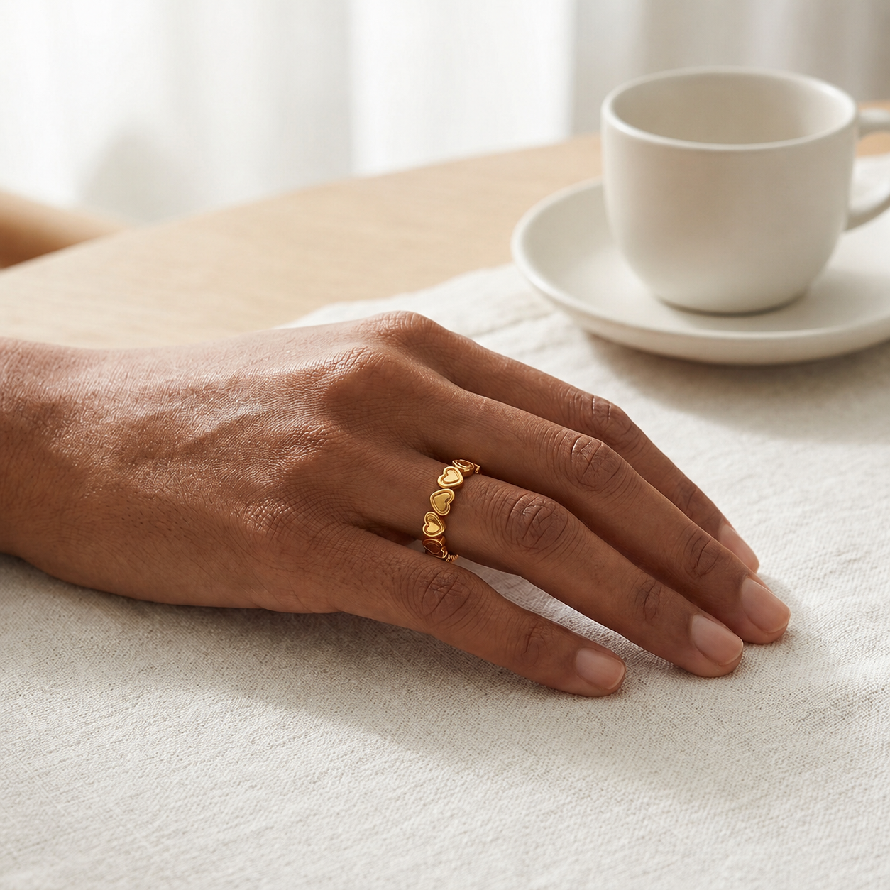 A close-up of a person's hand wearing a delicate gold ring with small heart charms.