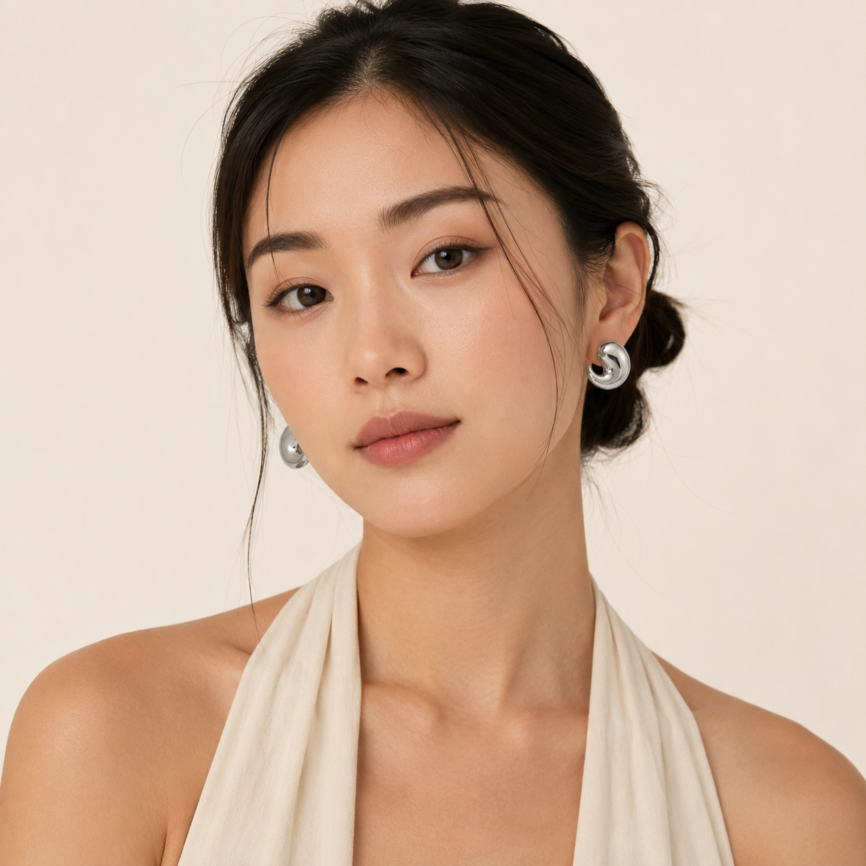 A woman with dark hair tied back wearing silver crescent-shaped stud earrings.