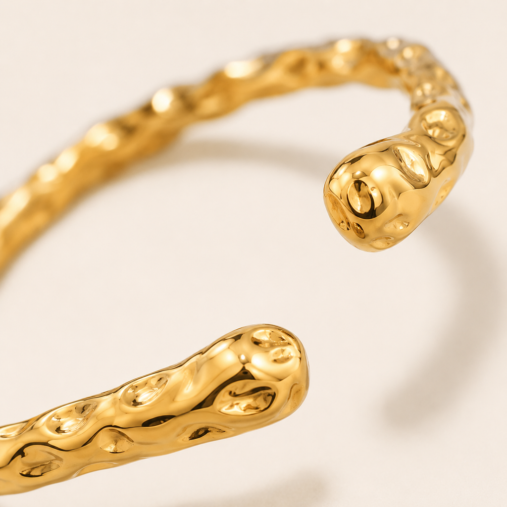 A close-up of a gold-toned textured bangle bracelet with an organic, wavy hammered finish.