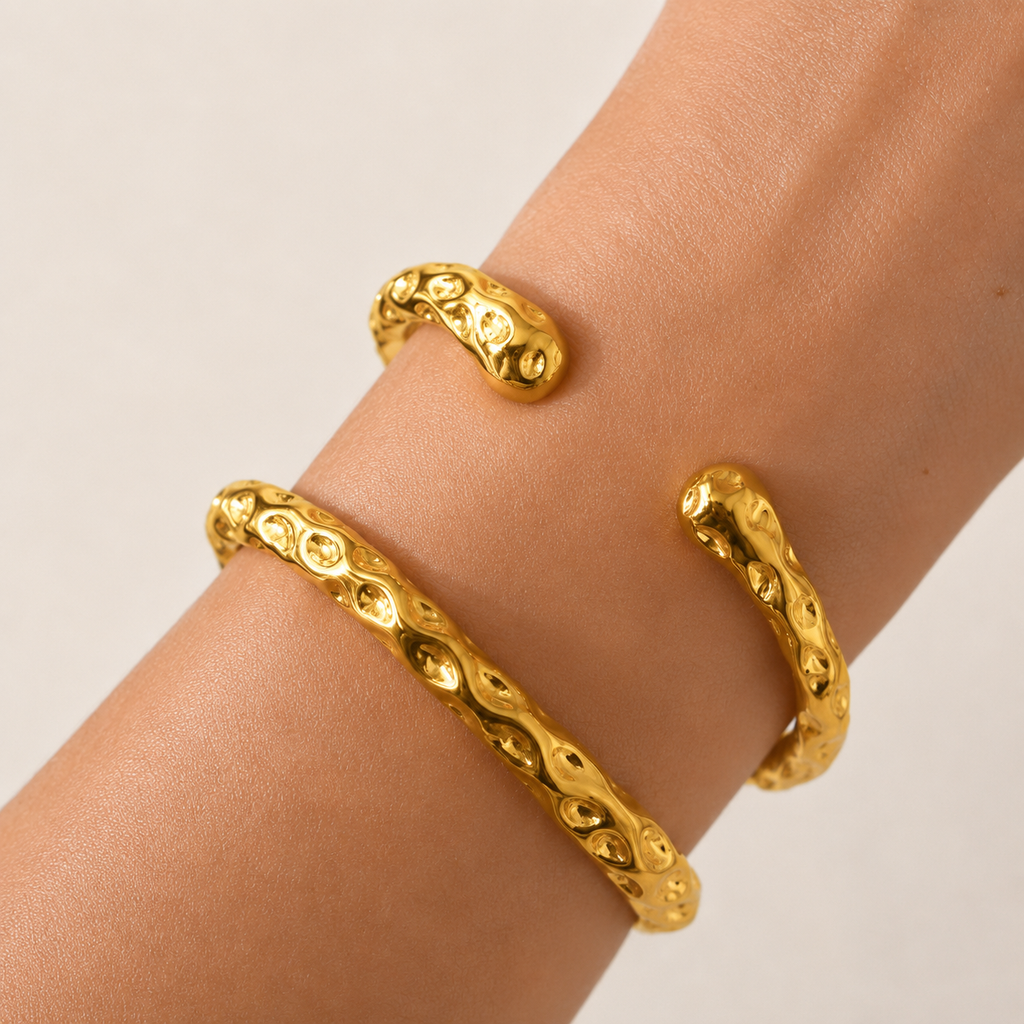 Two textured gold cuff bracelets worn on a person's wrist.