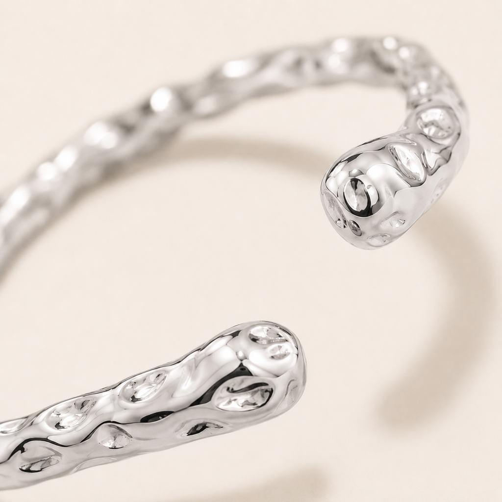 A close-up of a silver-toned textured bangle bracelet with an organic, wavy hammered finish.