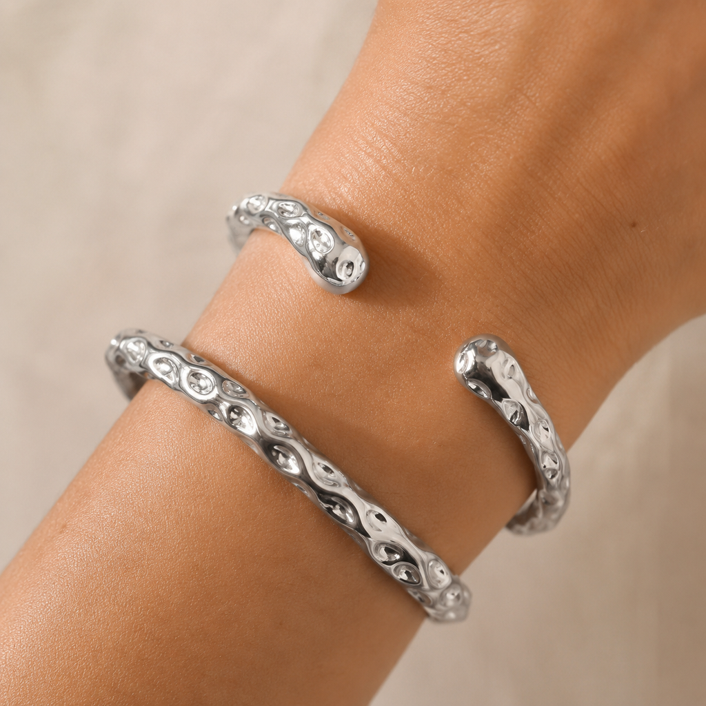 A close-up of a person's wrist wearing two silver open cuff bracelets with an intricate wavy pattern.