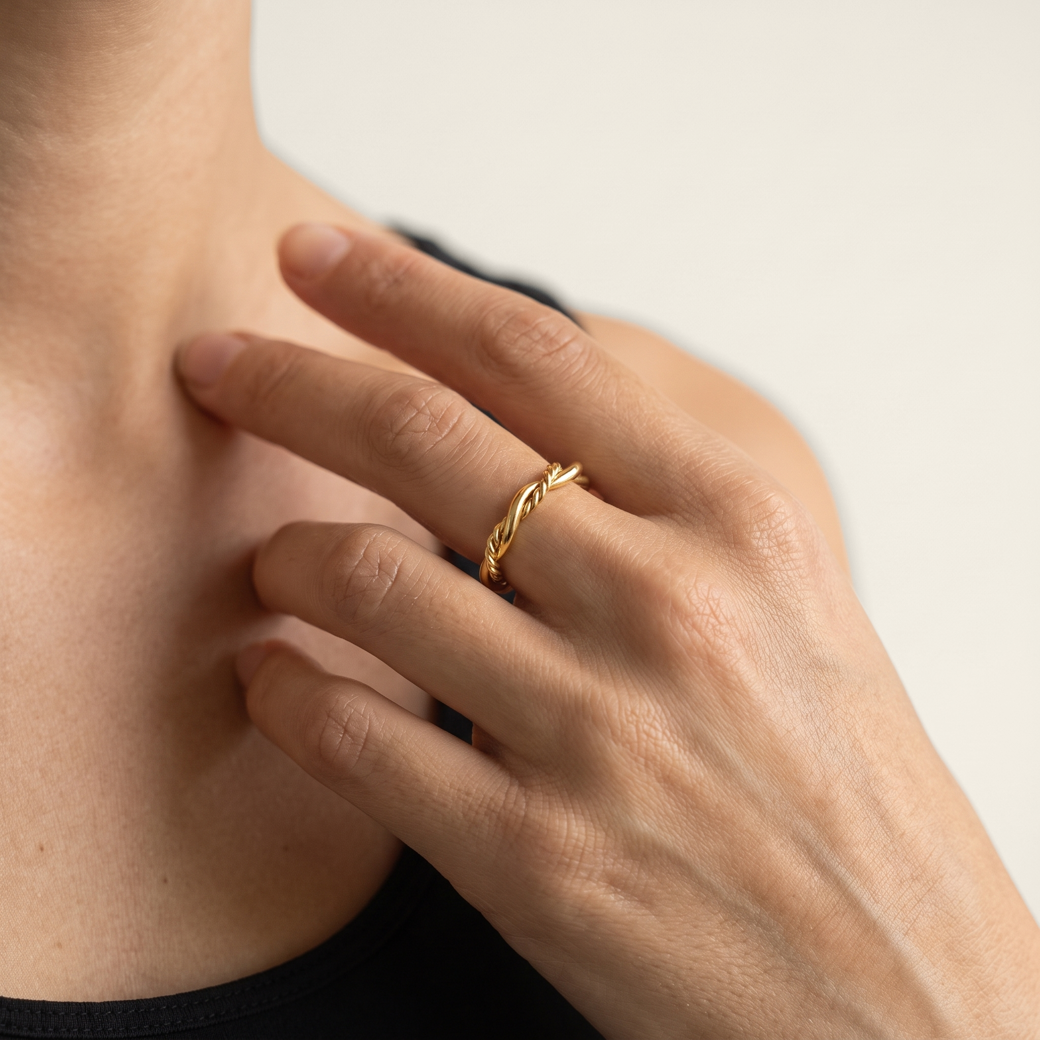 A close-up lifestyle shot of a person's hand wearing a thin, twisted rope style gold ring on their middle finger.