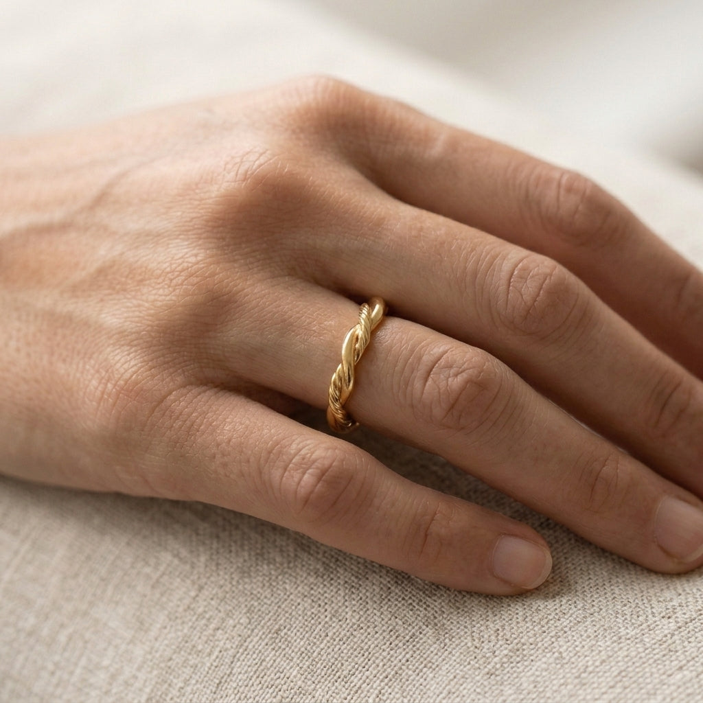 A close-up of a hand wearing a delicate twisted gold band ring on one finger.