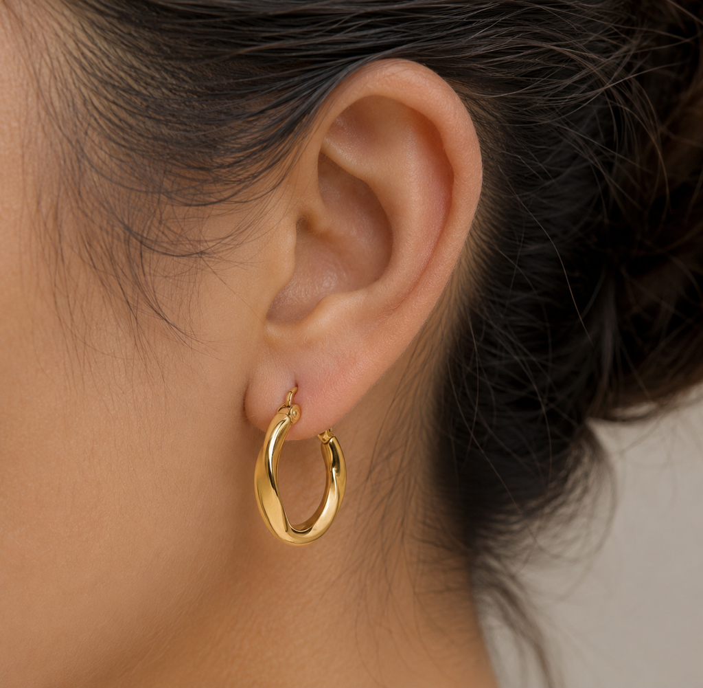 A close-up of a person's ear wearing a twisted gold hoop earring.