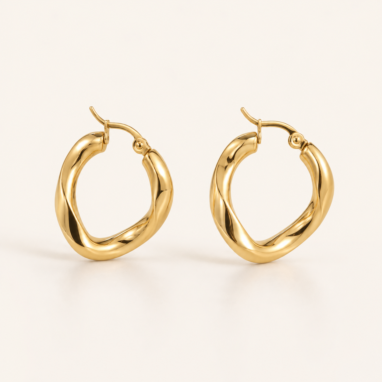 A pair of polished gold huggie hoop earrings with a twisted, organic design.