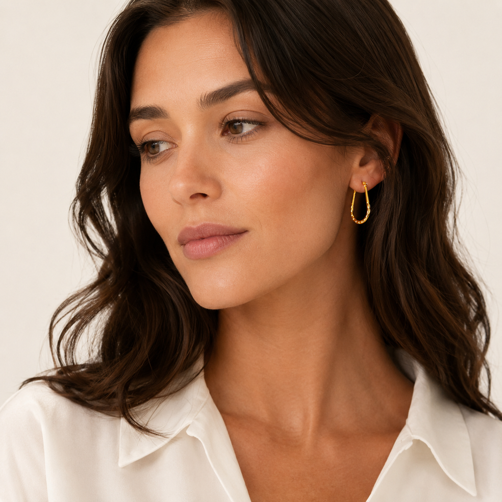 A close-up of a woman wearing a delicate pair of gold u-shaped earrings with a hammered finish.
