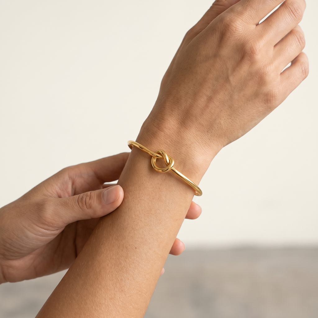 A gold-toned bangle bracelet with a love-knot center detail, shown worn on a person's wrist.