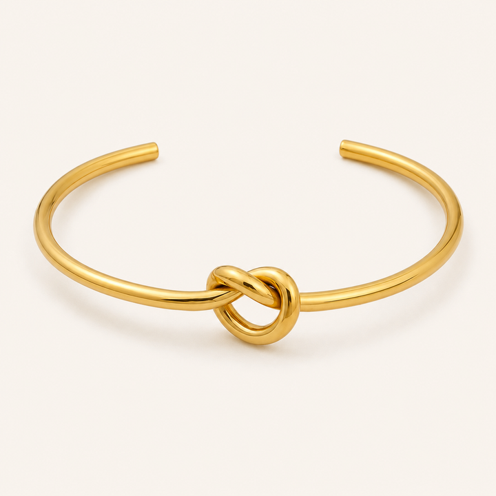 A polished gold open cuff bracelet featuring a central love-knot detail.