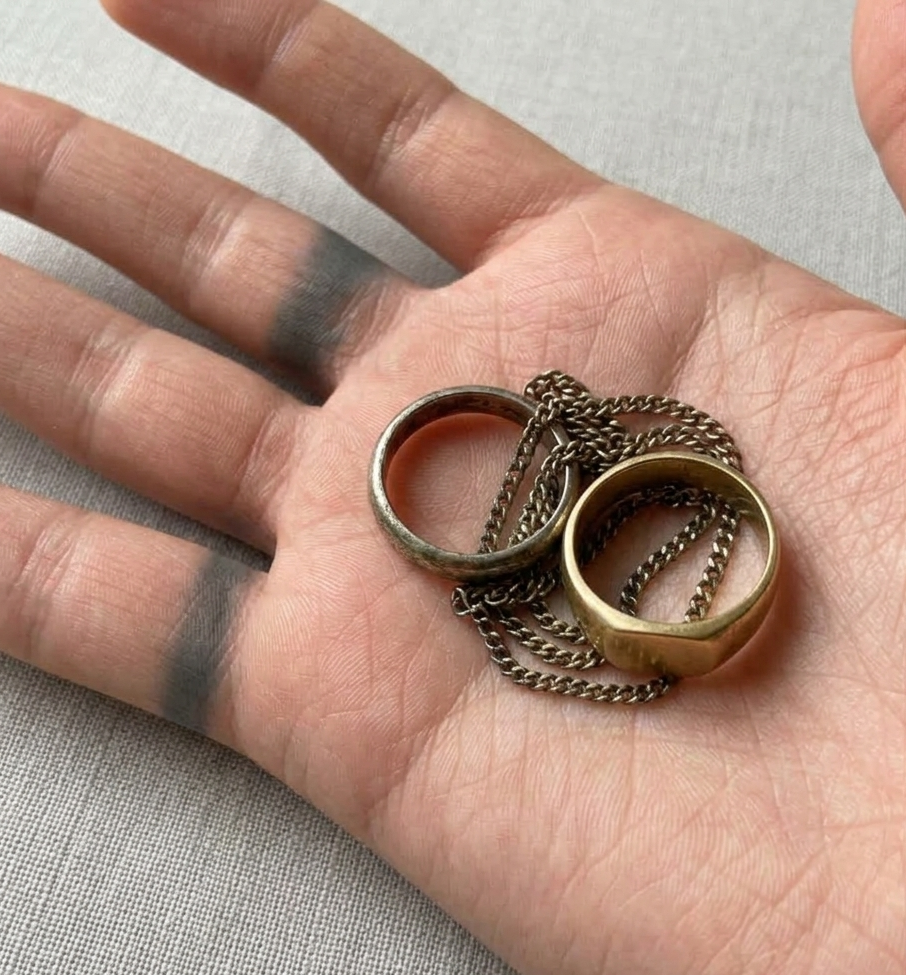 Hand holding two gold rings with chains on a neutral background