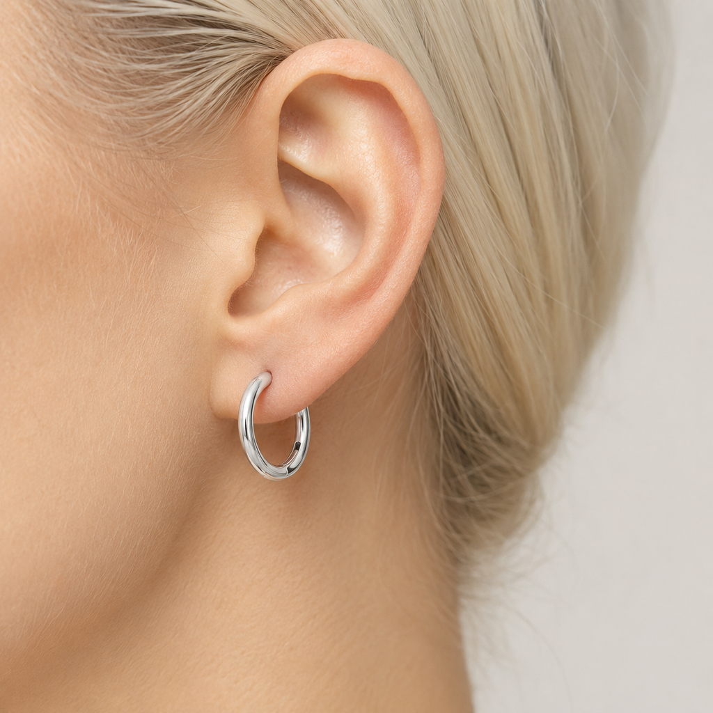 A close-up of a person's ear wearing a polished silver hoop earring.