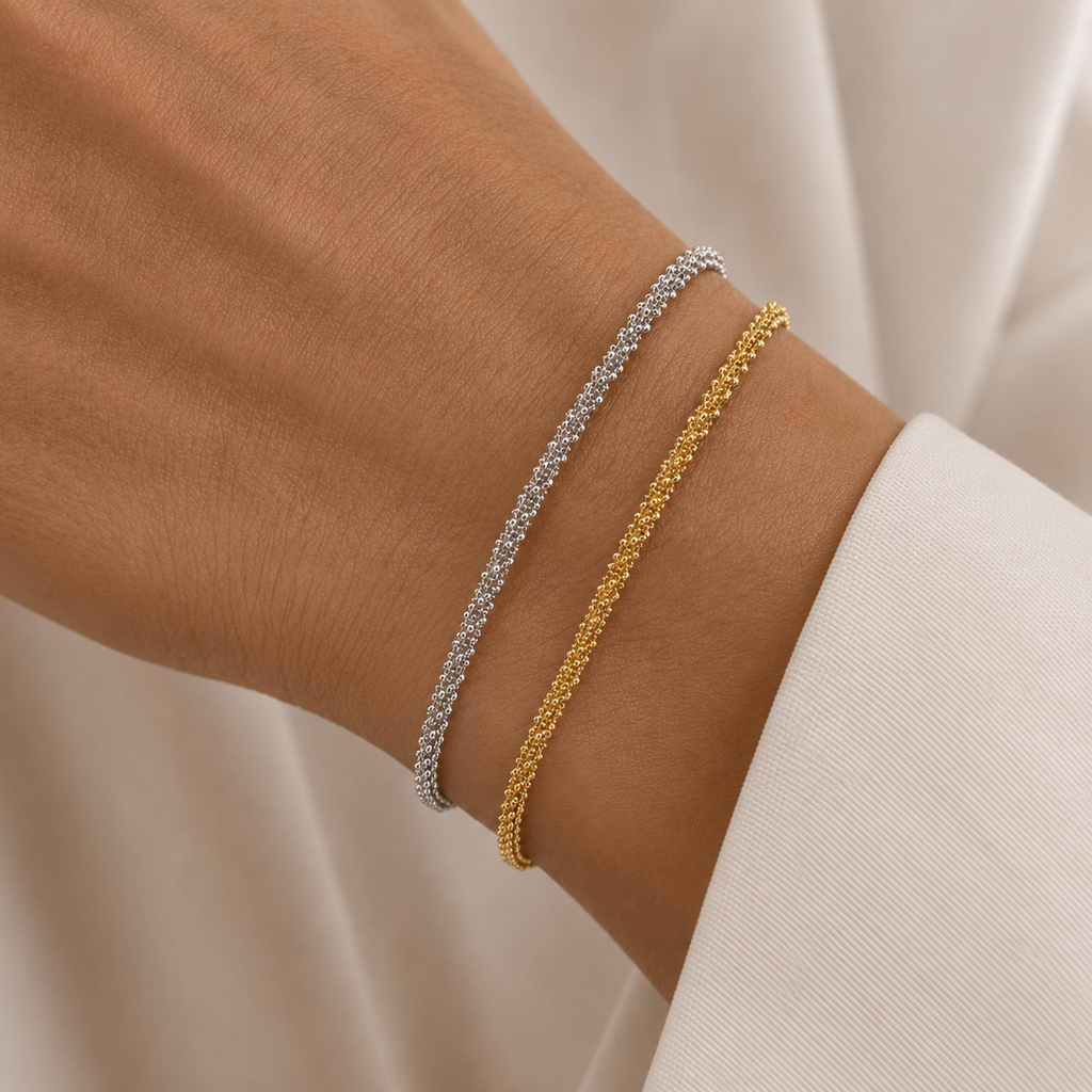 Two delicate woven-style bracelets on a person's wrist, one in silver and one in yellow gold.