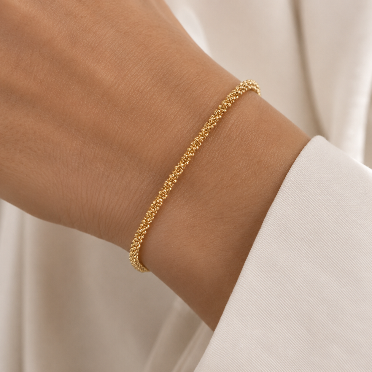 A delicate gold chain bracelet with a textured, woven appearance, shown worn on a person's wrist.