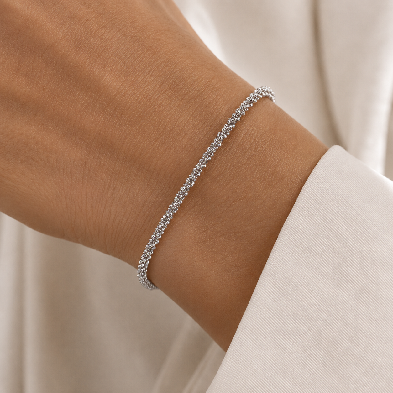 A delicate silver chain bracelet with a textured, woven appearance, shown worn on a person's wrist.