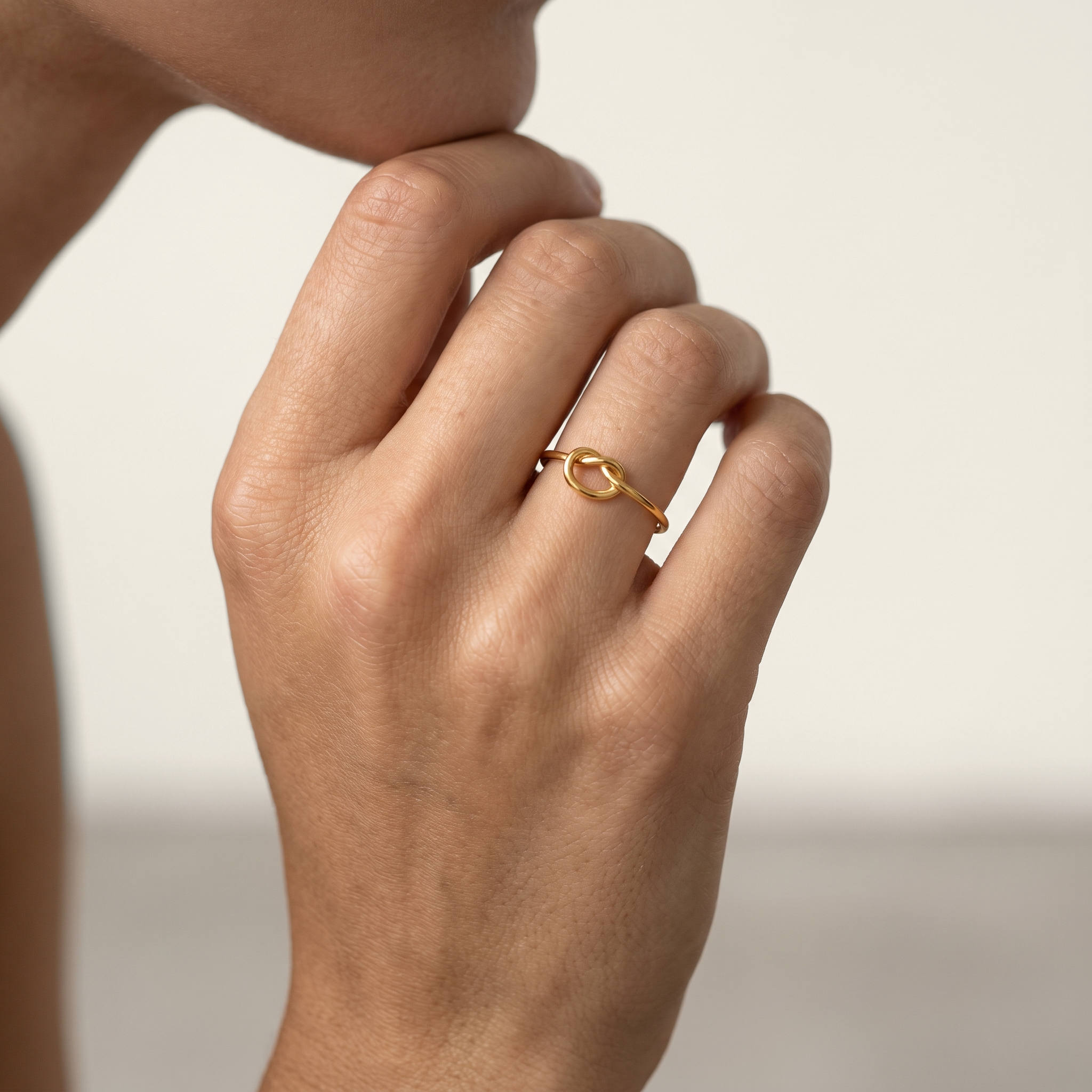 A close-up of a person's hand wearing a delicate gold ring with a small oval love-knot.