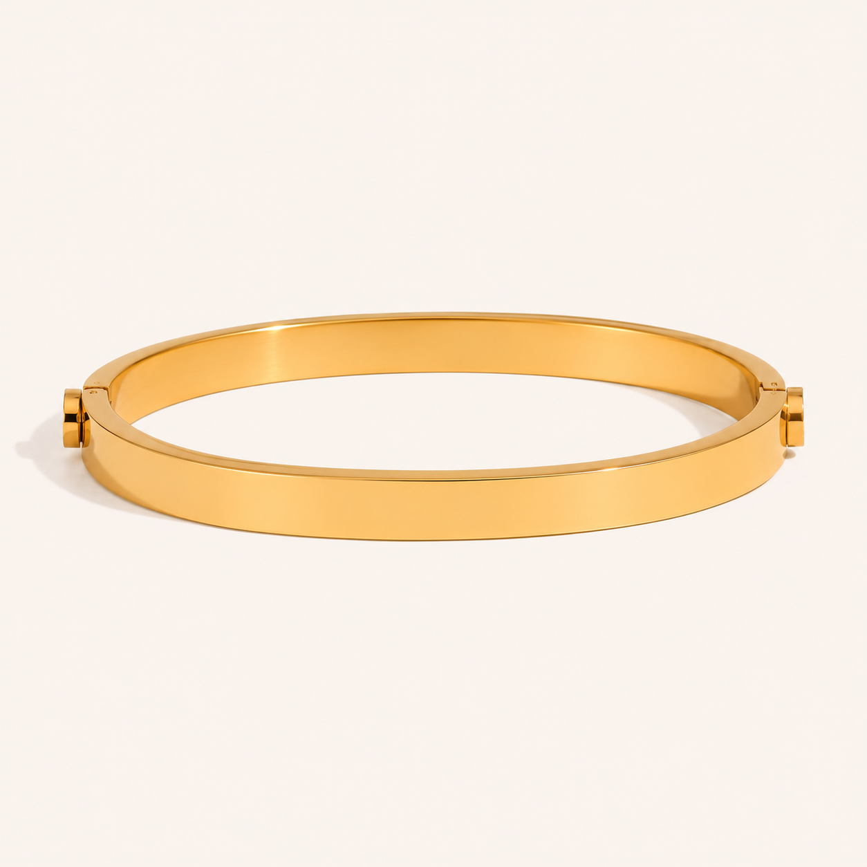 A polished gold bangle bracelet with a flat, wide band and small decorative end details.