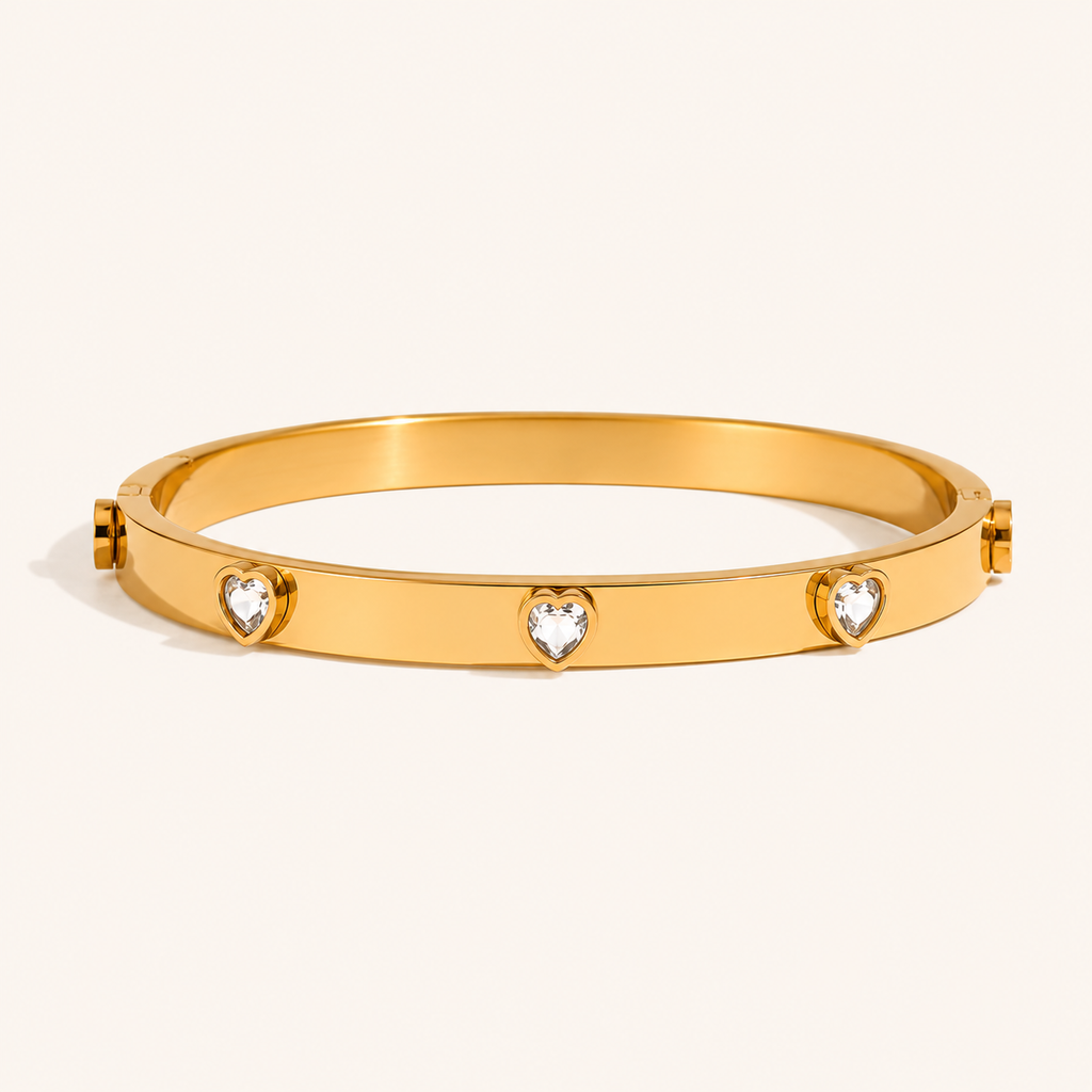 A polished gold bangle bracelet featuring four small heart-shaped clear gemstone zircons spaced evenly around the band.