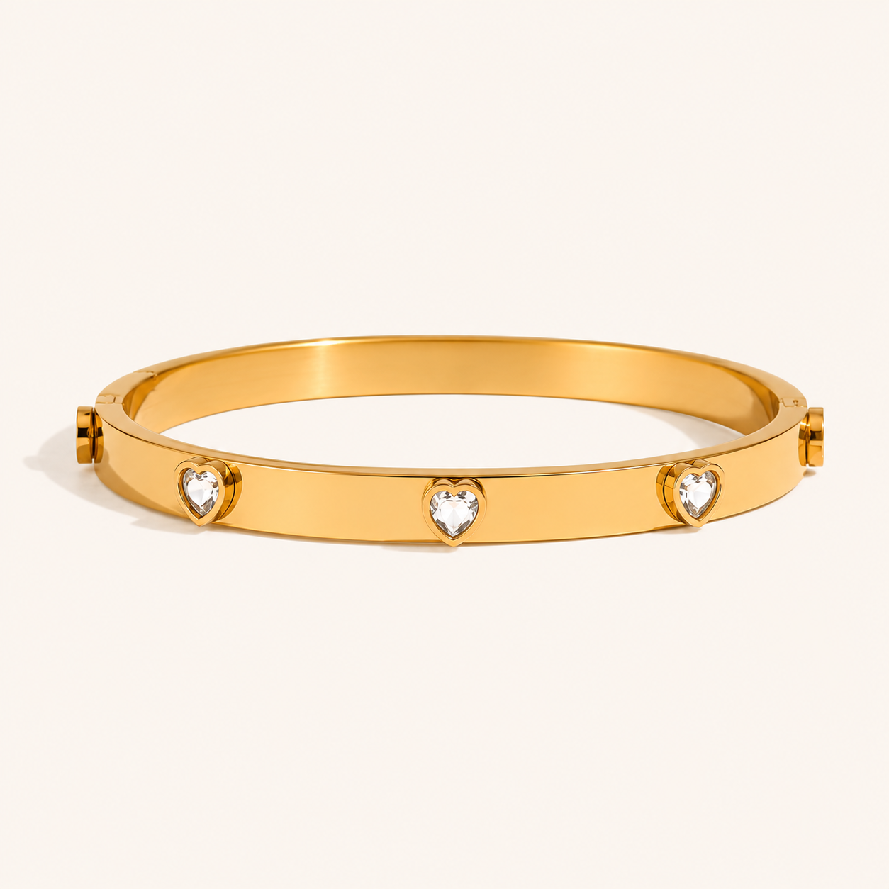 A polished gold bangle bracelet featuring four small heart-shaped clear gemstone zircons spaced evenly around the band.