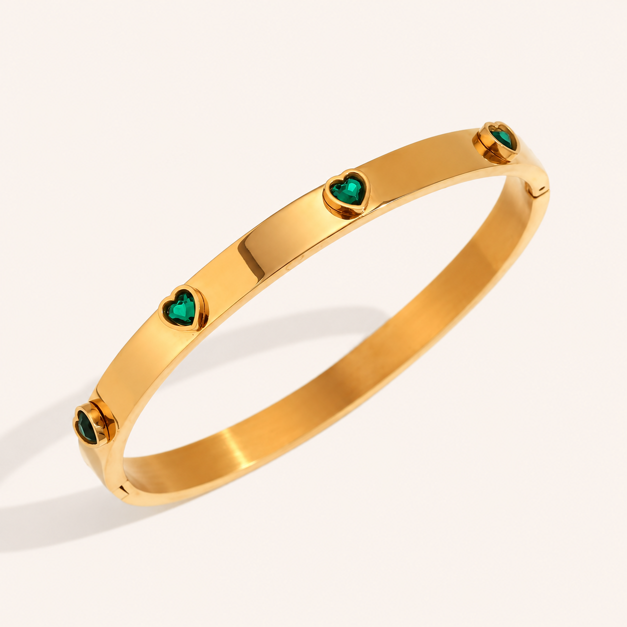 A polished gold bangle bracelet featuring four small heart-shaped green gemstone zircons spaced evenly around the band.