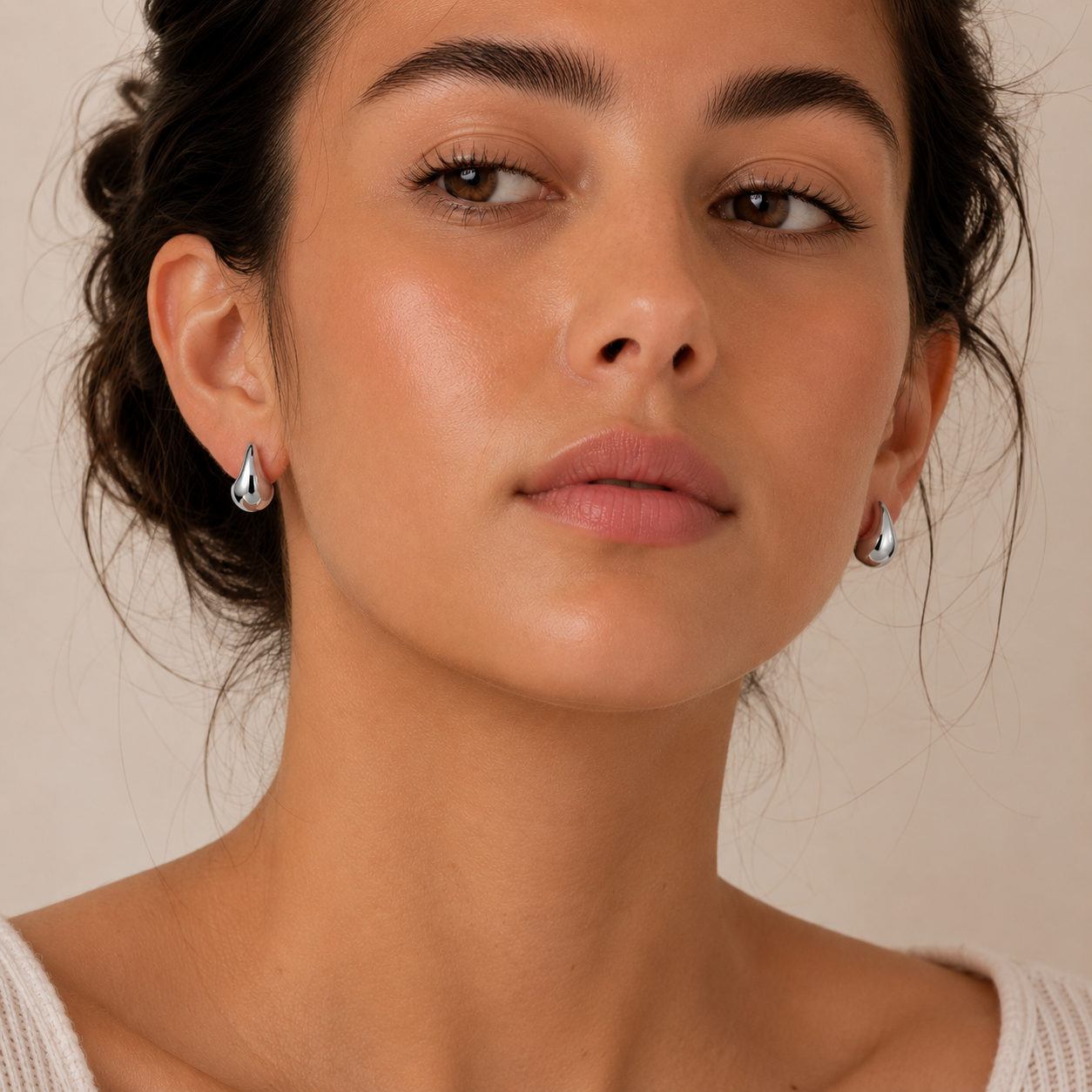 A close-up portrait of a woman wearing small silver teardrop-shaped earrings.