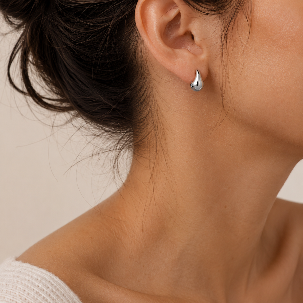 A close-up of a woman's ear wearing a small silver teardrop-shaped stud earring.