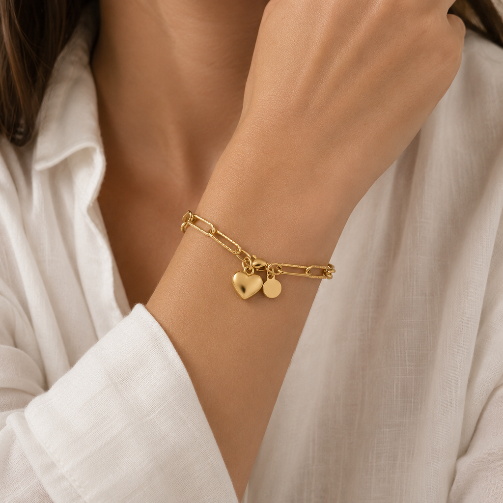 A delicate gold chain bracelet with a small heart charm, worn on a woman's wrist.