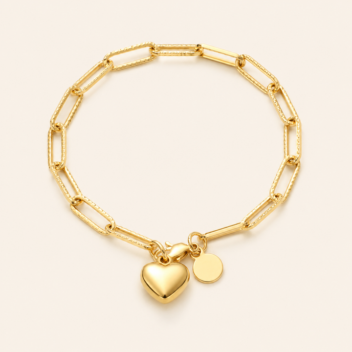 A gold paperclip chain bracelet with a polished heart charm and a small round disc charm.