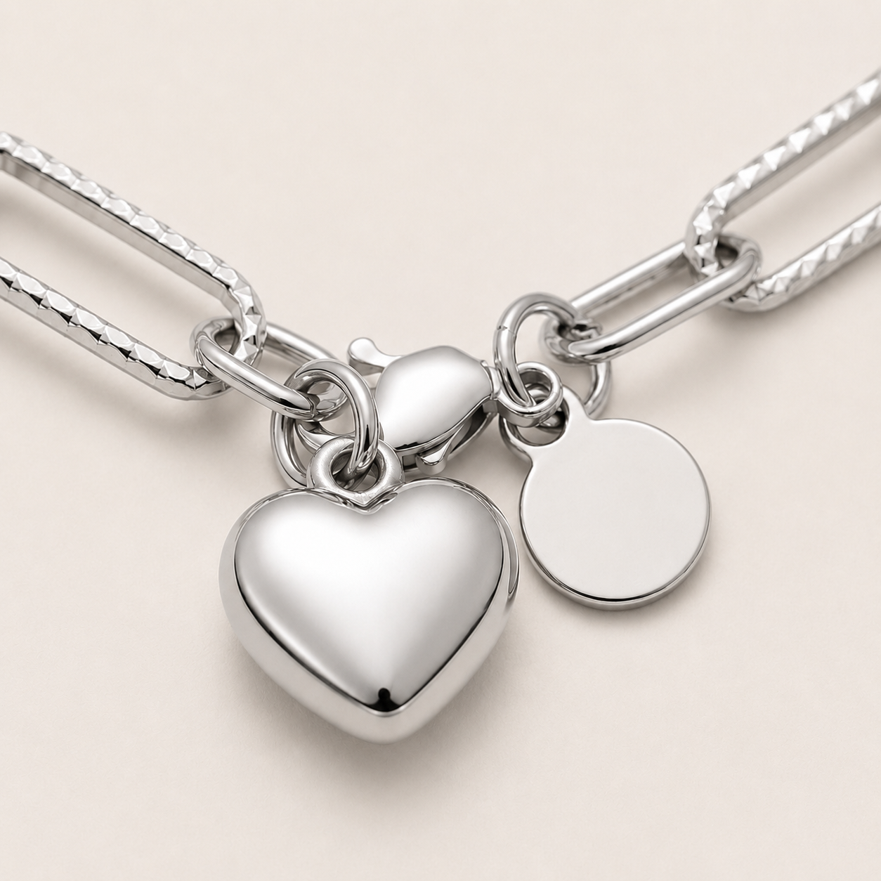 A close-up of a silver chain necklace with a large polished heart charm and a blank round disc tag.