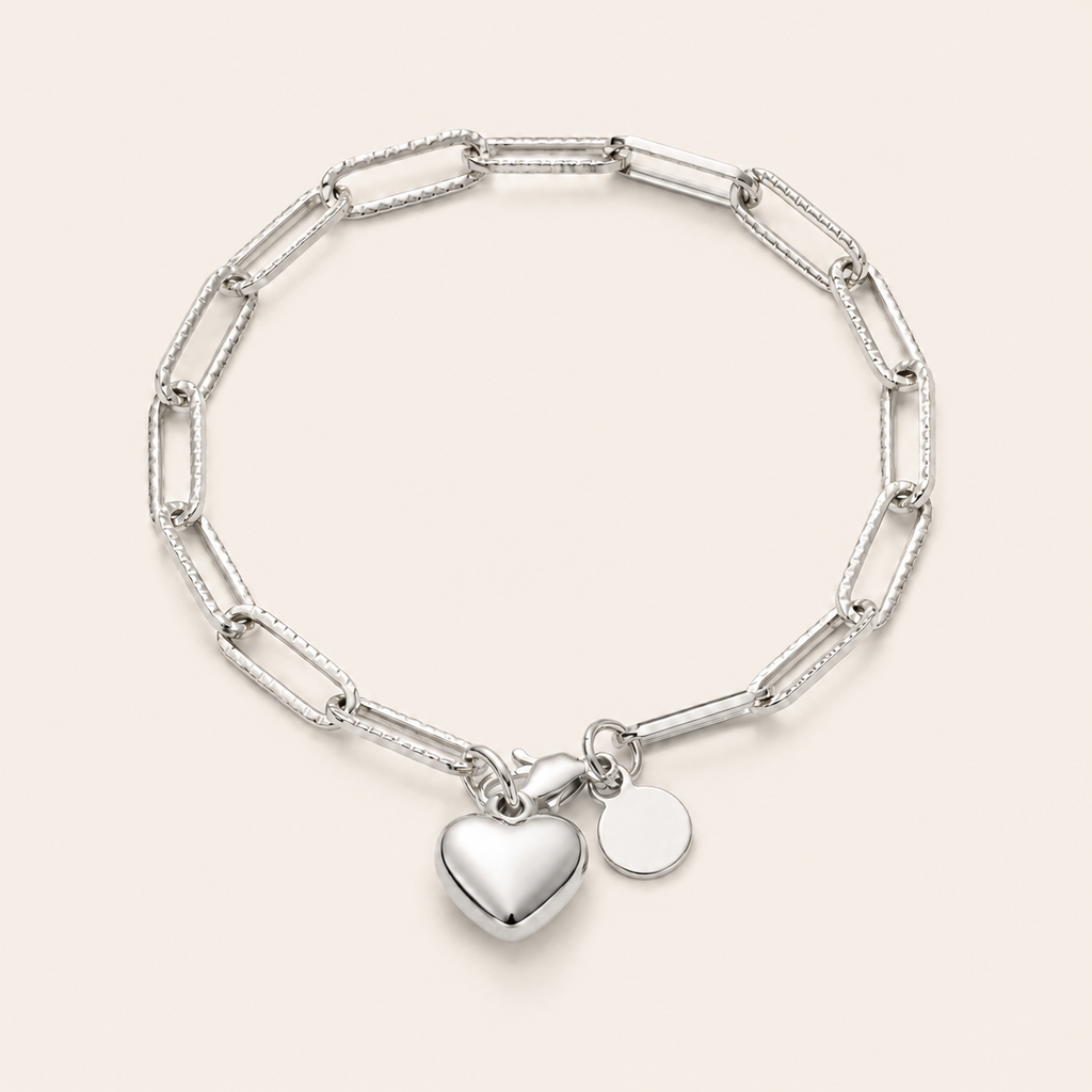A silver paperclip chain bracelet with a polished heart charm and a small round disc charm.