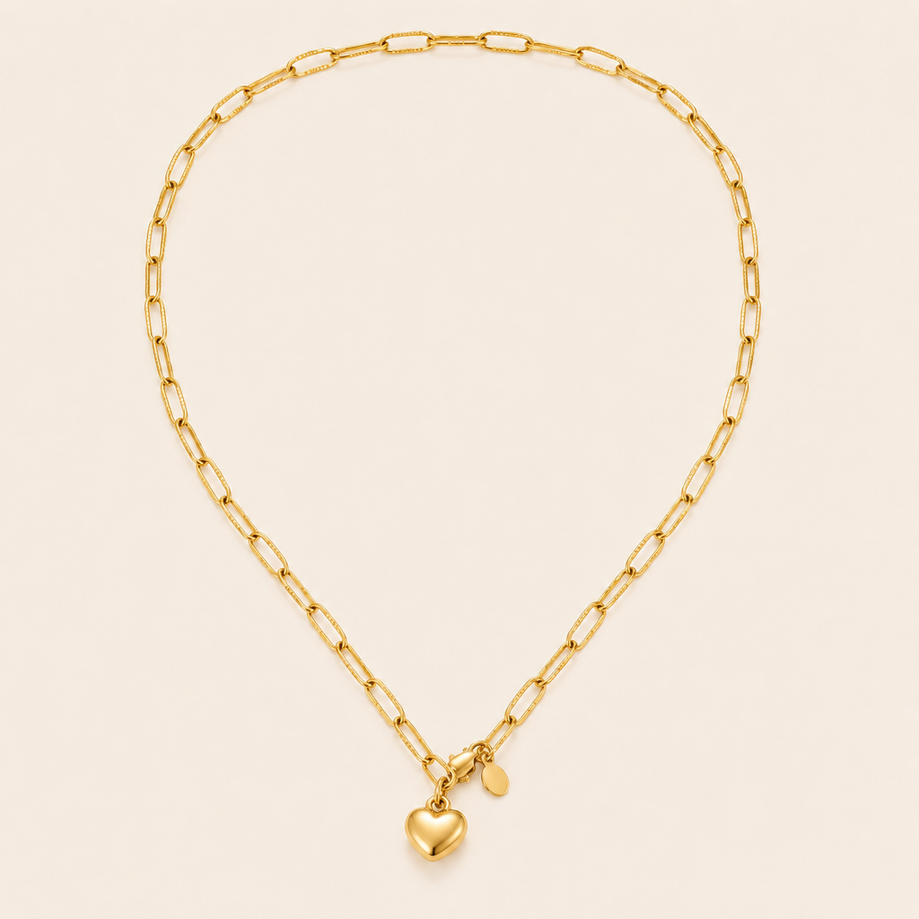 A gold paperclip chain necklace with a small polished heart charm and a tiny oval tag.