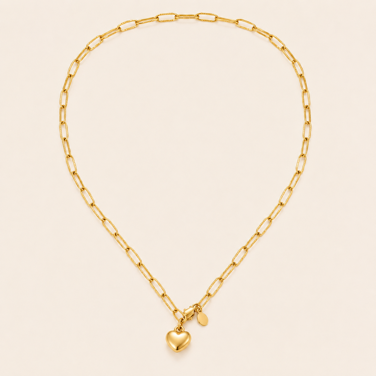 A gold paperclip chain necklace with a small polished heart charm and a tiny oval tag.