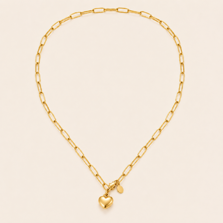 A gold paperclip chain necklace with a small polished heart charm and a tiny oval tag.