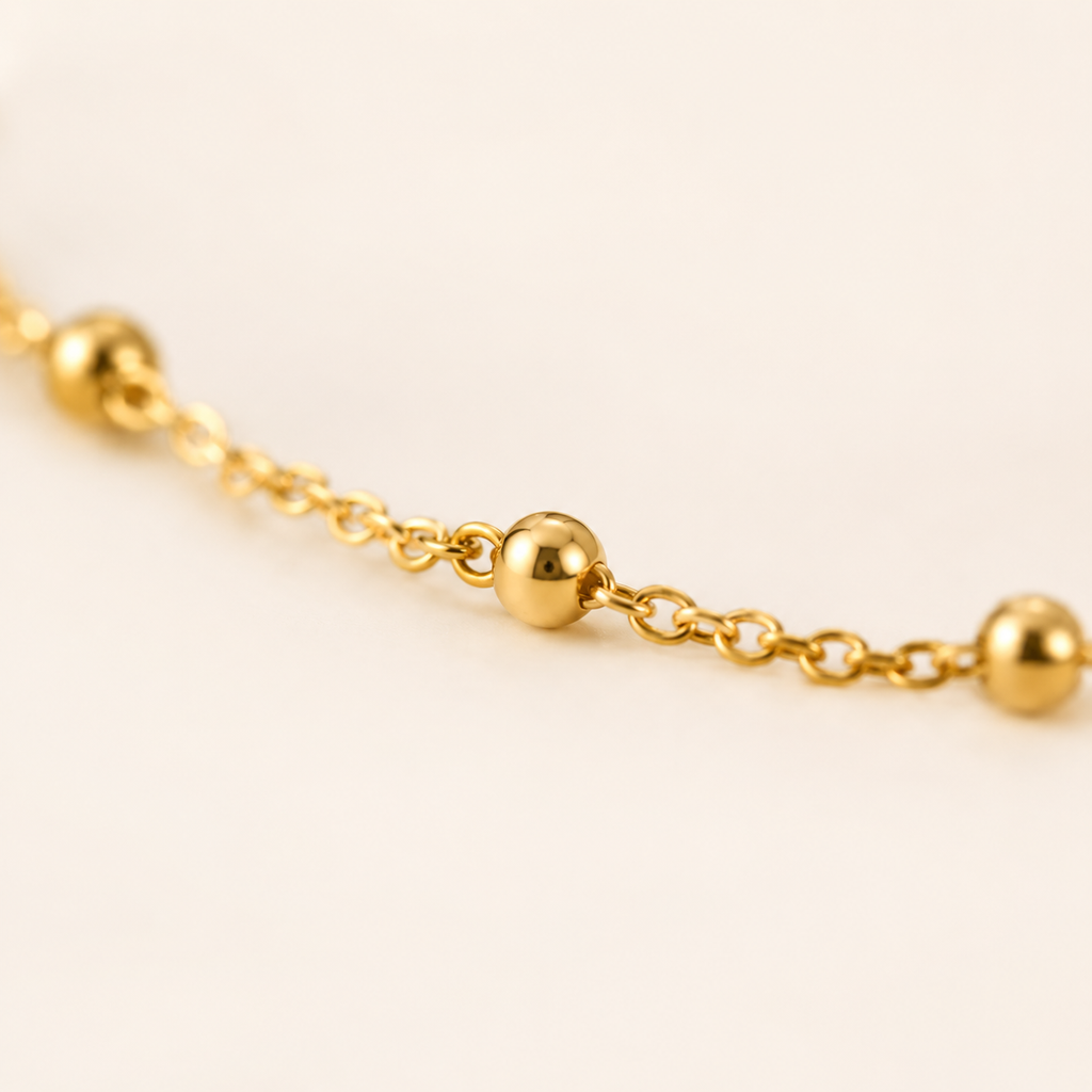 A close-up of a delicate gold chain anklet featuring evenly spaced, polished spherical beads.