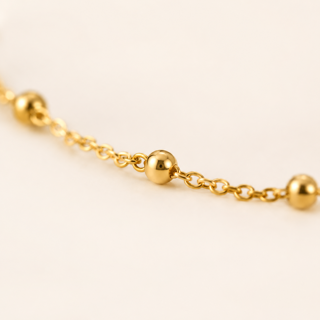 A close-up of a delicate gold chain anklet featuring evenly spaced, polished spherical beads.