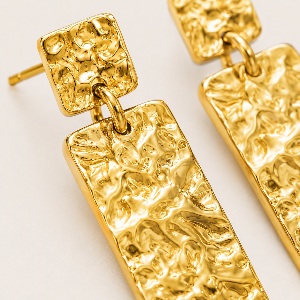 Close-up of textured gold drop earrings with square textured studs and long rectangular dangling bars.
