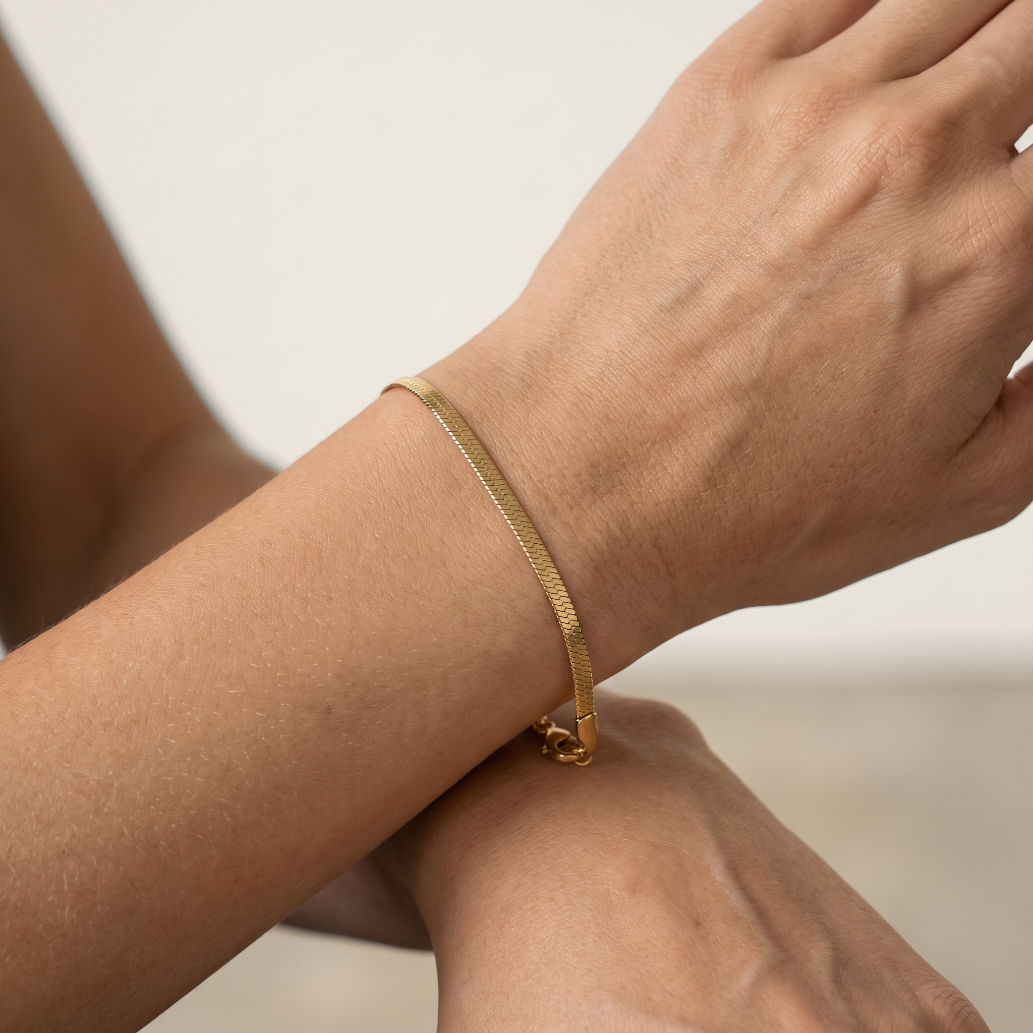 A close-up of a delicate gold herringbone chain bracelet, worn on a person's wrist.