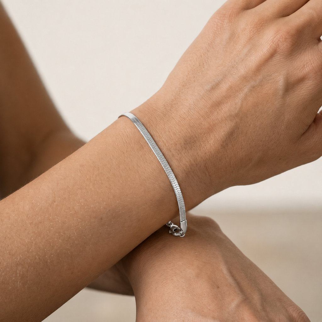 A close-up of a person's wrist wearing a slim silver snake chain bracelet.
