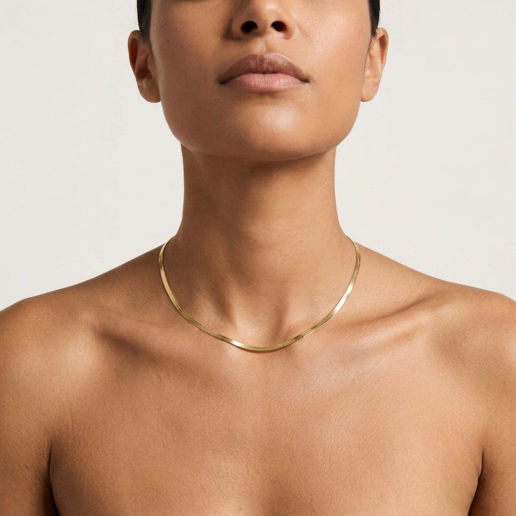 A close-up of a model wearing a delicate, thin gold herringbone chain necklace.