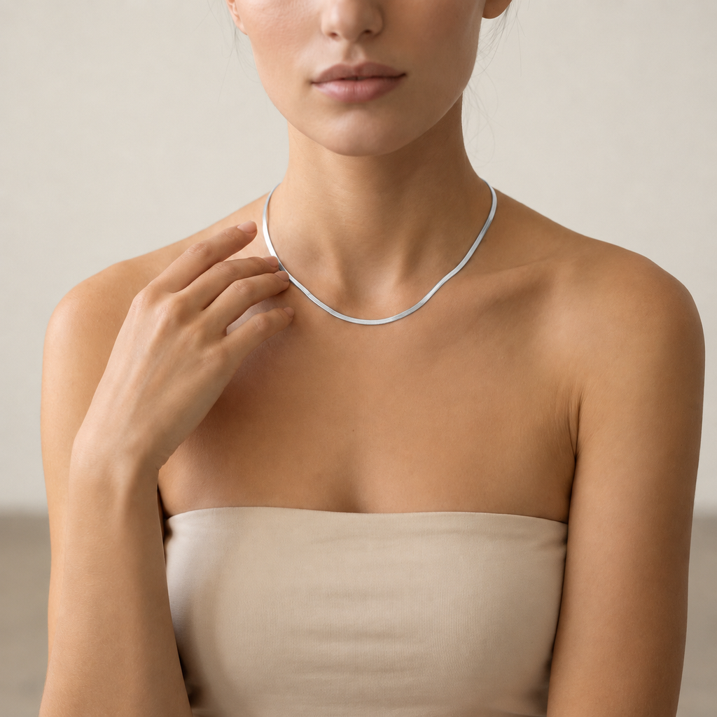 A close-up of a woman wearing a delicate silver herringbone chain necklace.
