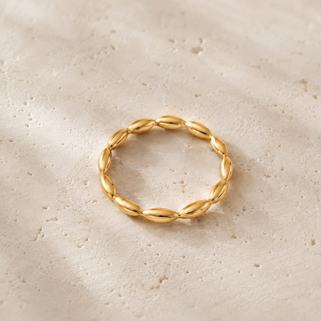 A single gold ring with a textured, twisted oval design, resting on a stone textured surface.