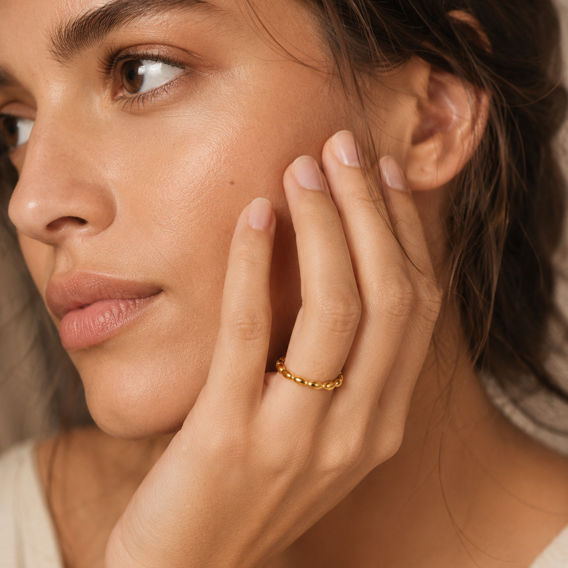 A close-up lifestyle shot of a woman wearing a delicate, thin gold ring with beaded twisted design, on her finger.