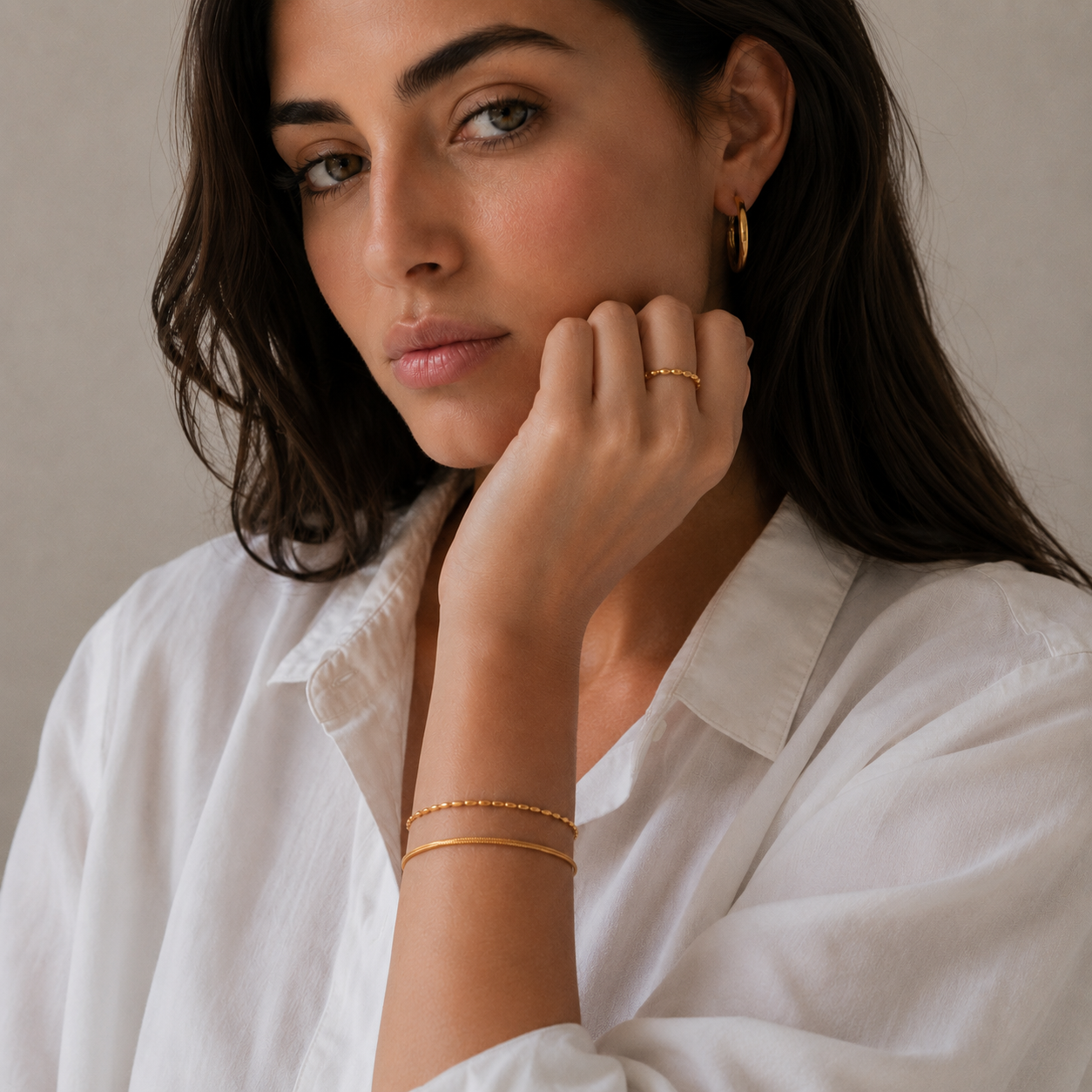 A close-up lifestyle shot of a woman wearing delicate gold jewelry, including a gold beaded bracelet and a gold ring.