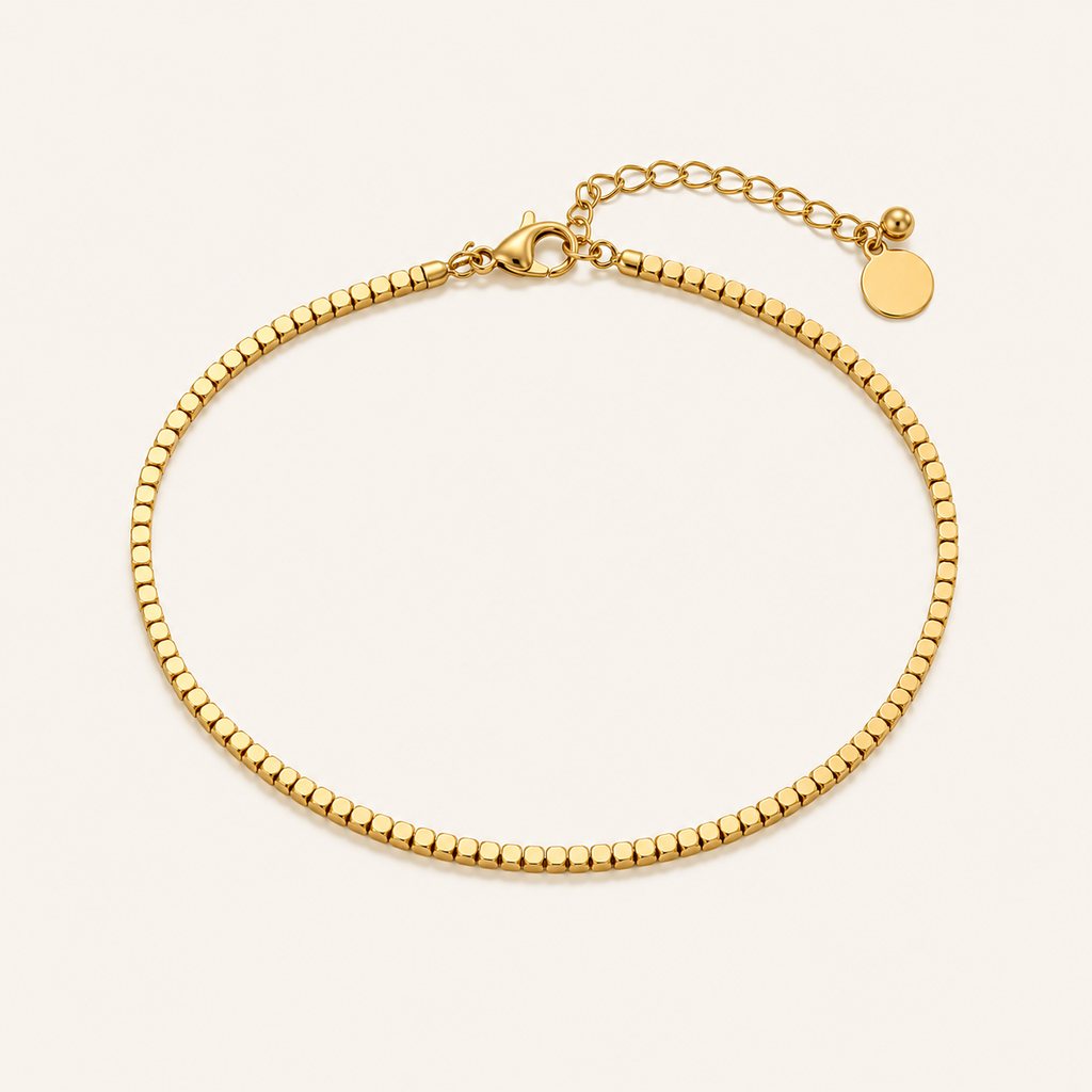 A gold beaded chain anklet with a lobster clasp, and extender chain, displayed on a light cream background.