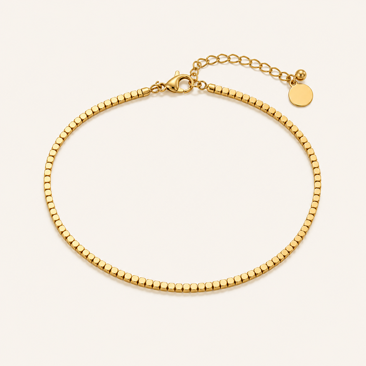 A gold beaded chain anklet with a lobster clasp, and extender chain, displayed on a light cream background.