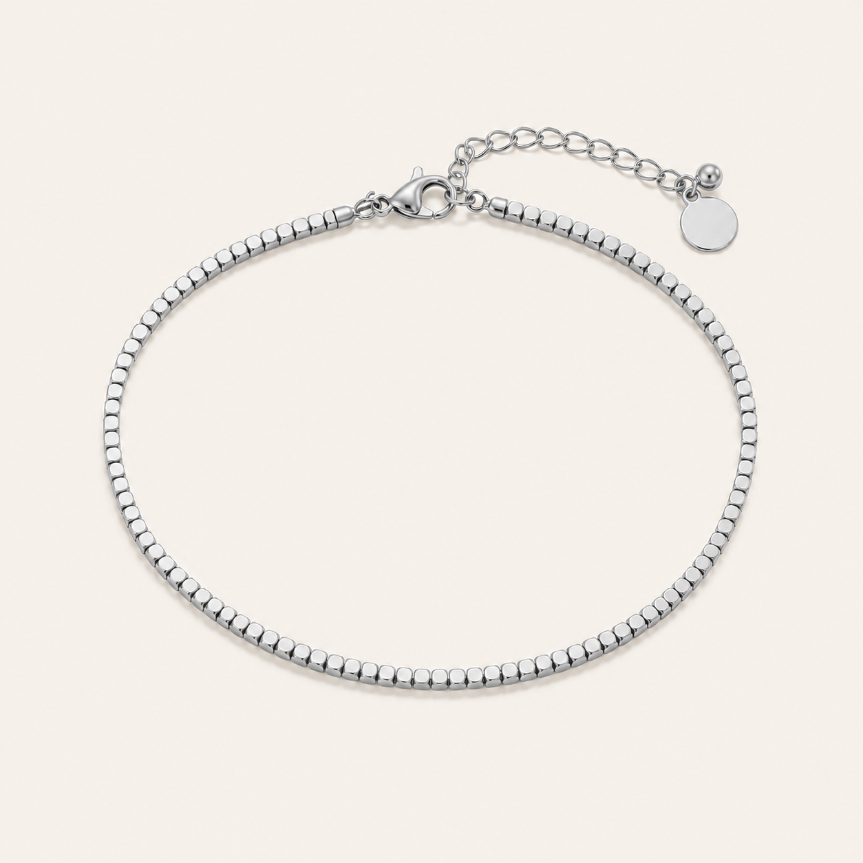 A silver beaded anklet with a lobster clasp, and extender chain, displayed on a light beige background.