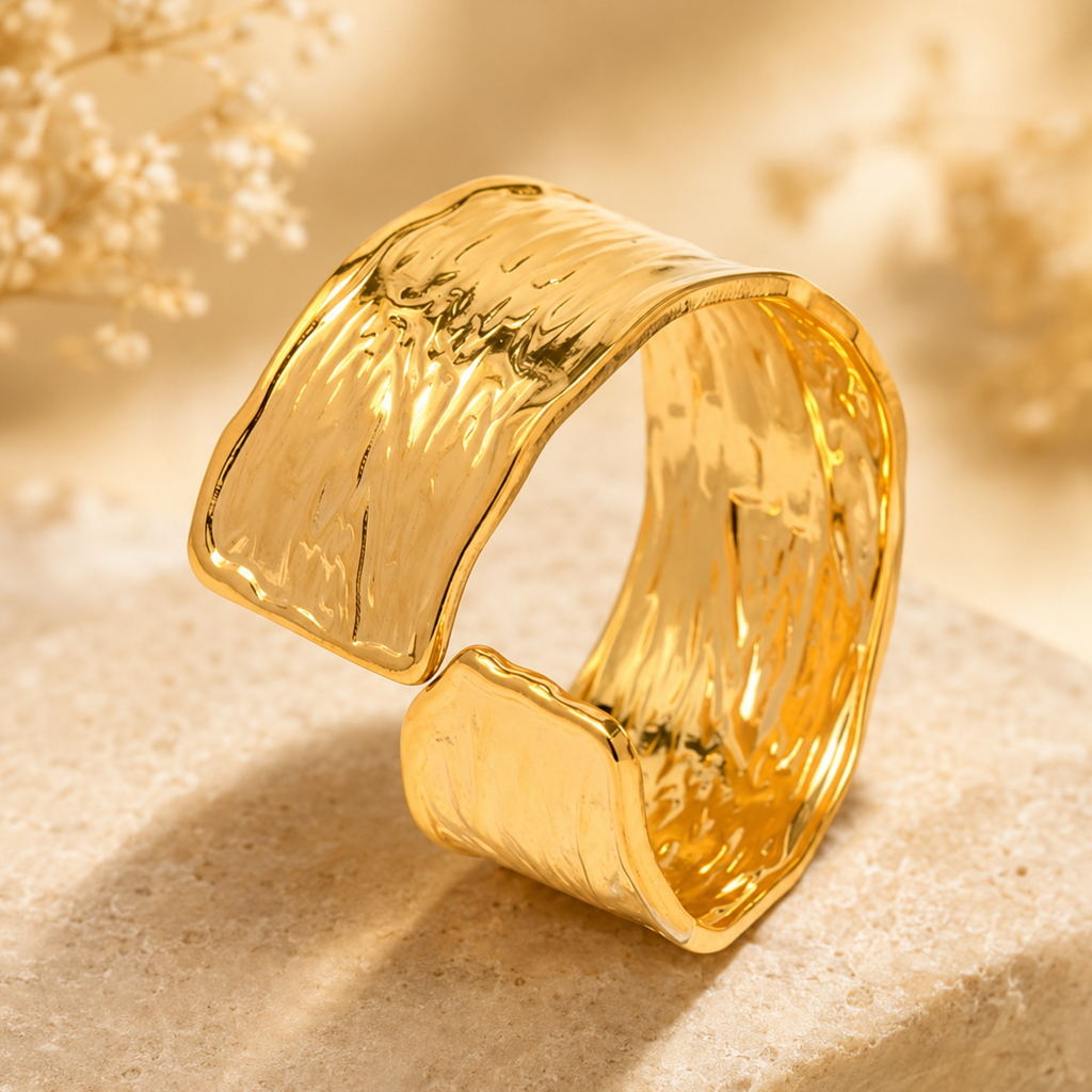 A wide, open cuff ring in polished yellow gold with a textured, hammered surface.