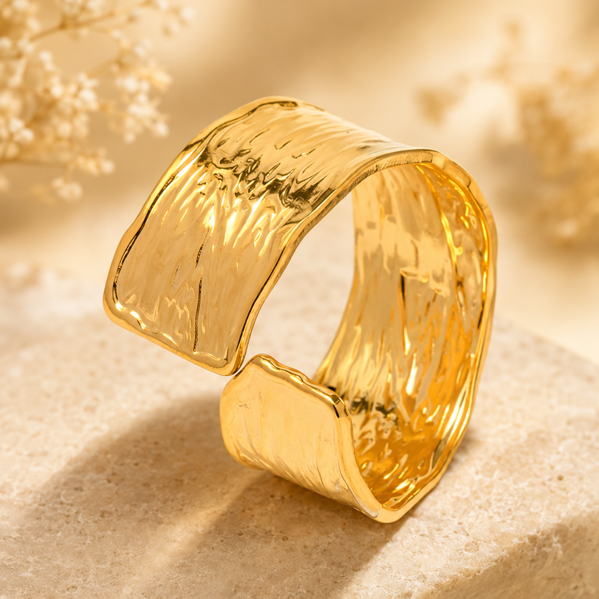 A wide, open cuff ring in polished yellow gold with a textured, hammered surface.
