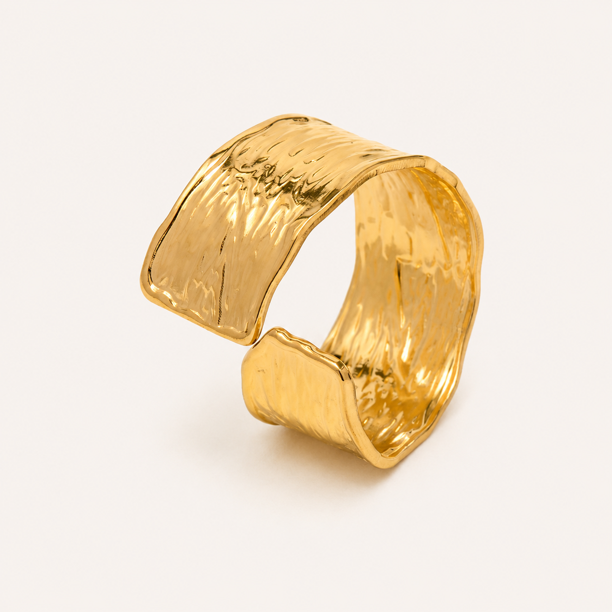 A wide, open cuff ring in textured yellow gold with a hammered, organic surface finish.