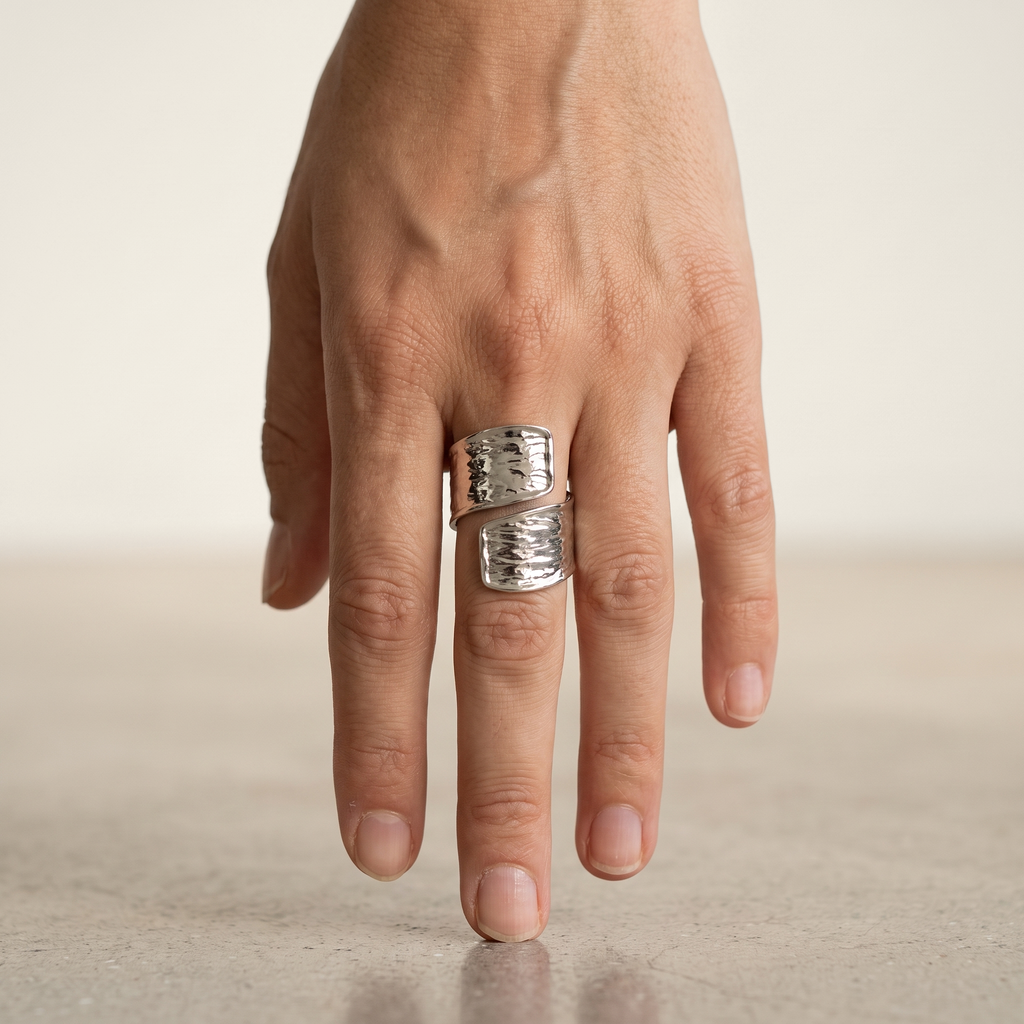 A close-up of a hand wearing a wide silver wrap ring with a textured, hammered finish.