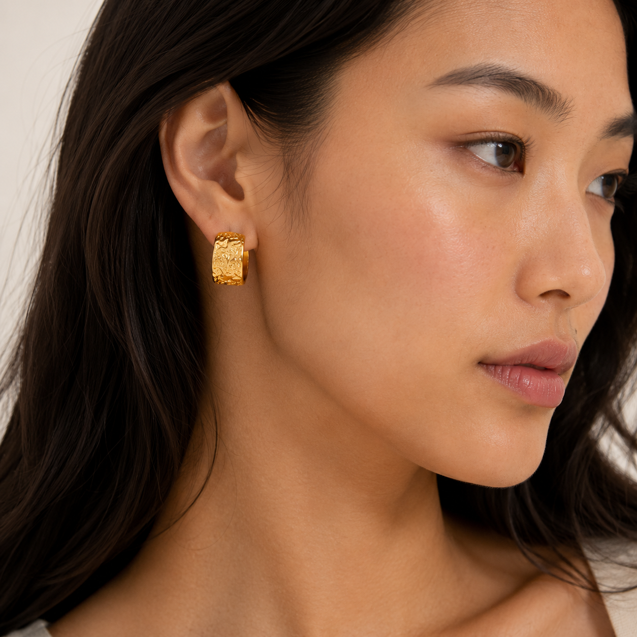 A close-up of a woman wearing a textured gold hoop earring.